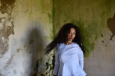 Portrait of woman with tousled hair standing against wall