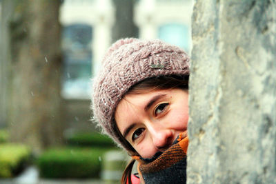 Close-up portrait of woman in knit hat hiding by wall