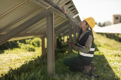 Side view of female engineer examining solar panels while kneeling at power station