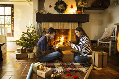 Couple wrapping gift boxes on floor by fireplace at home