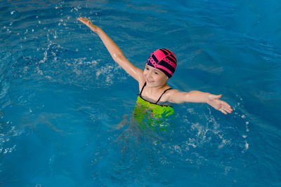 High angle view of girl with arms outstretched swimming in pool