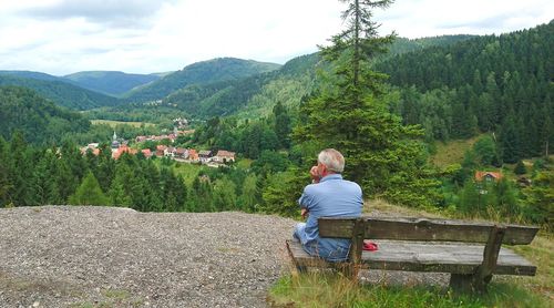 Rear view of man sitting on wooden bench at lautenthal