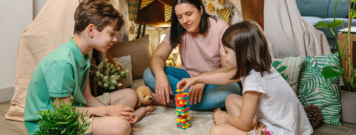 Banner of happy family having fun playing together with wooden stacking piece game on living room