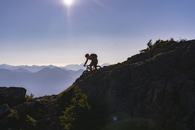 Hiker riding bicycle on mountain against sky