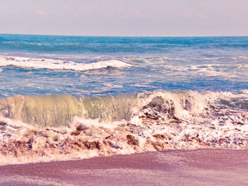 Waves rushing towards shore against sky