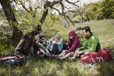 Happy friends looking at map while sitting on grassy field