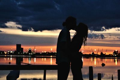 Silhouette couple standing by river against sky at night