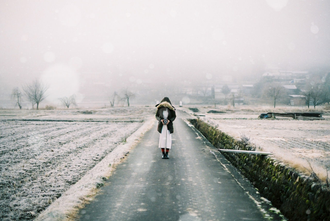 FULL LENGTH REAR VIEW OF MAN WALKING ON ROAD DURING WINTER