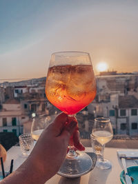 Close-up of hand holding drink against sky during sunset