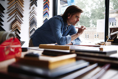 Mature male store owner using laptop leaning on table while working in store