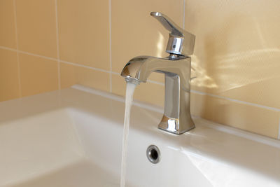 Modern faucet in yellow bathroom with running water, close up, side view. concept hygiene
