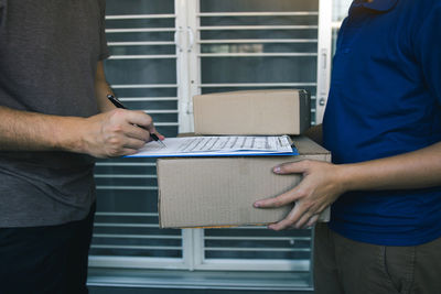 Midsection of man customer signing while delivery person holding package