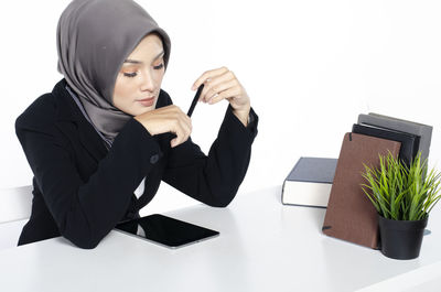 Young woman sitting on table against white background