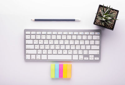 Directly above shot of computer keyboard with office supplies and plant over white background