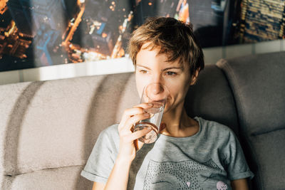 Portrait of a short-haired young woman drinking water from a glass