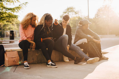 Multi-ethnic friends looking at smart phone while sitting at skateboard park