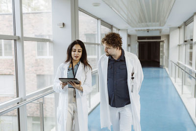 Female doctor discussing over digital tablet with male colleague while walking together in hospital corridor