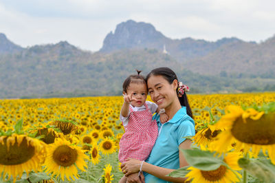 Portrait of mother and daughter standing amidst sunflowers
