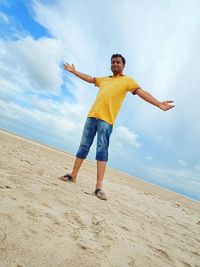 Portrait of man standing with arms outstretched at shore of beach against sky