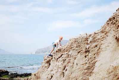 Little boy walking on rocks beach against sky