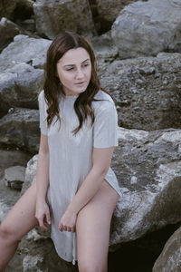 Beautiful young woman sitting on rock at shore