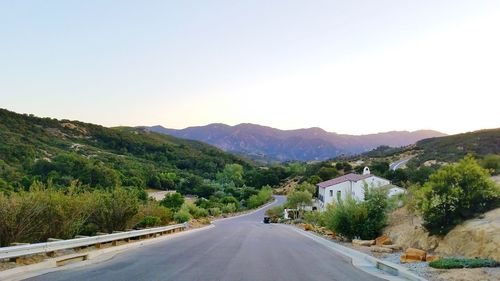 Road leading towards mountains against clear sky