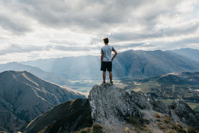 Rear view of man standing on mountain against sky