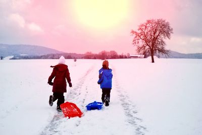 Rear view of siblings with sled running on snow against sky