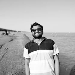 Portrait of smiling man standing at beach against clear sky
