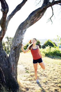 Young woman exercising by tree trunk on grassy field