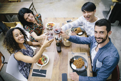 High angle portrait of young friends toasting wineglasses at restaurant