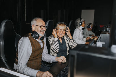 Smiling senior couple playing video game by male and female friends in gaming lounge