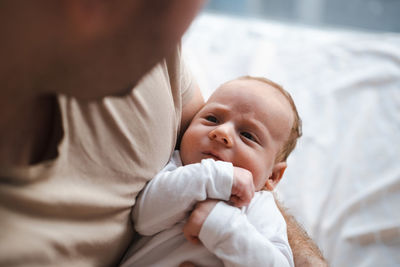 Portrait of cute baby boy lying in father hands looking at him at home