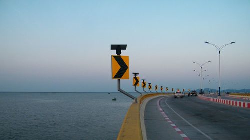 Road sign on street by sea against clear sky