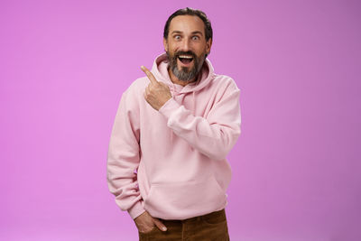 Portrait of man pointing against purple background