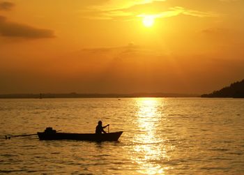 Silhouette man sailing boat on sea against sky during sunset