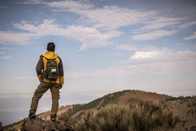 Rear view of mature man with backpack standing on mountain against sky