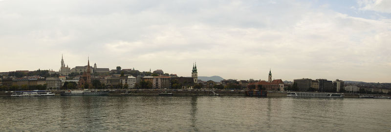 View of buildings by river against cloudy sky