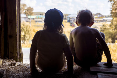 Rear view of siblings sitting on hay in wooden barn