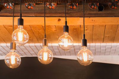 Close-up of illuminated light bulb hanging on ceiling