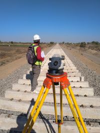 Engineer standing by theodolite outdoors against sky