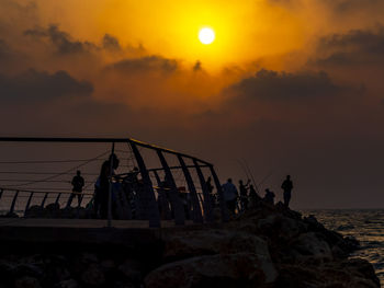 Silhouette people by sea against sky during sunset