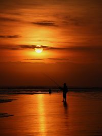 Silhouette person fishing in sea against orange sky during sunset