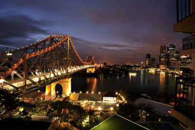 Illuminated bridge over river in city against sky at night