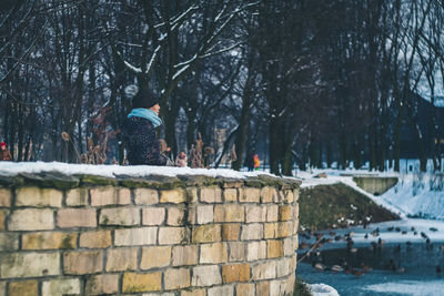Girl standing by stone wall during winter