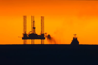 Silhouette cranes at construction site against orange sky