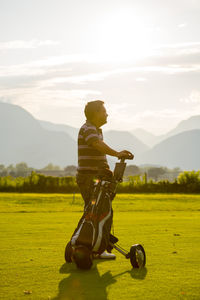 Man standing with golf bag against sky during sunset