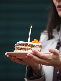 Woman holding birthday cake with a birthday candle on a beige plate