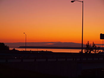 Silhouette street by sea against orange sky