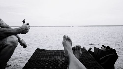 Low section of men relaxing on beach against sky